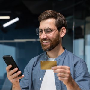 Cheerful and smiling bearded businessman doing online shopping and bank money transfer, freelancer